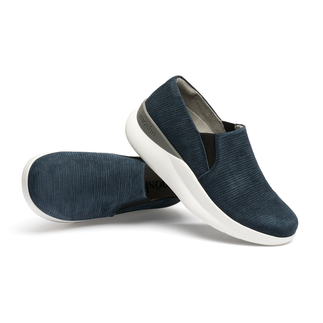 A pair of navy blue suede slip-on shoes with a white sole.