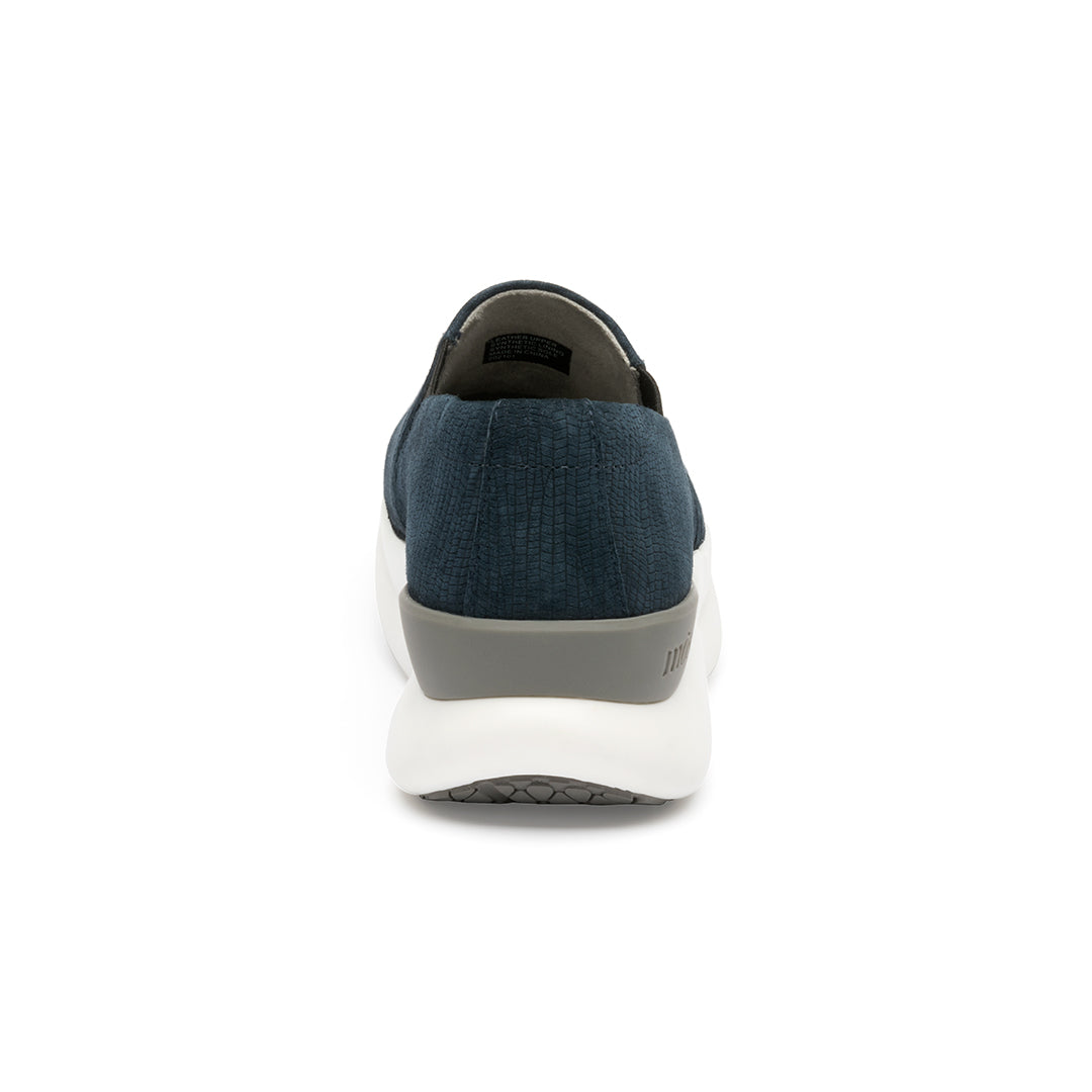 A pair of navy blue suede slip-on shoes with a white sole. Back view
